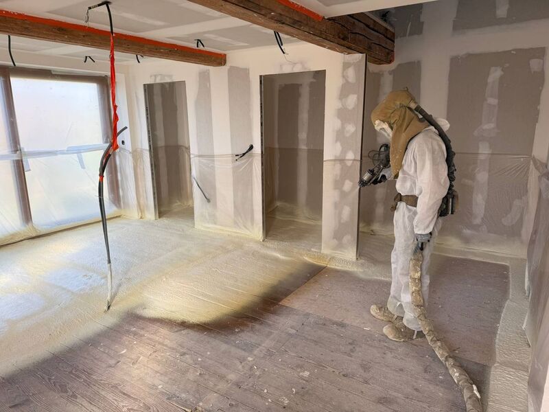 Technicien isolant un sol à la mousse polyuréthane projetée — vue large du chantier